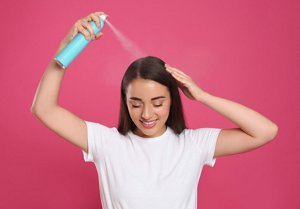 Brunette woman spraying her hair with a dry shampoo